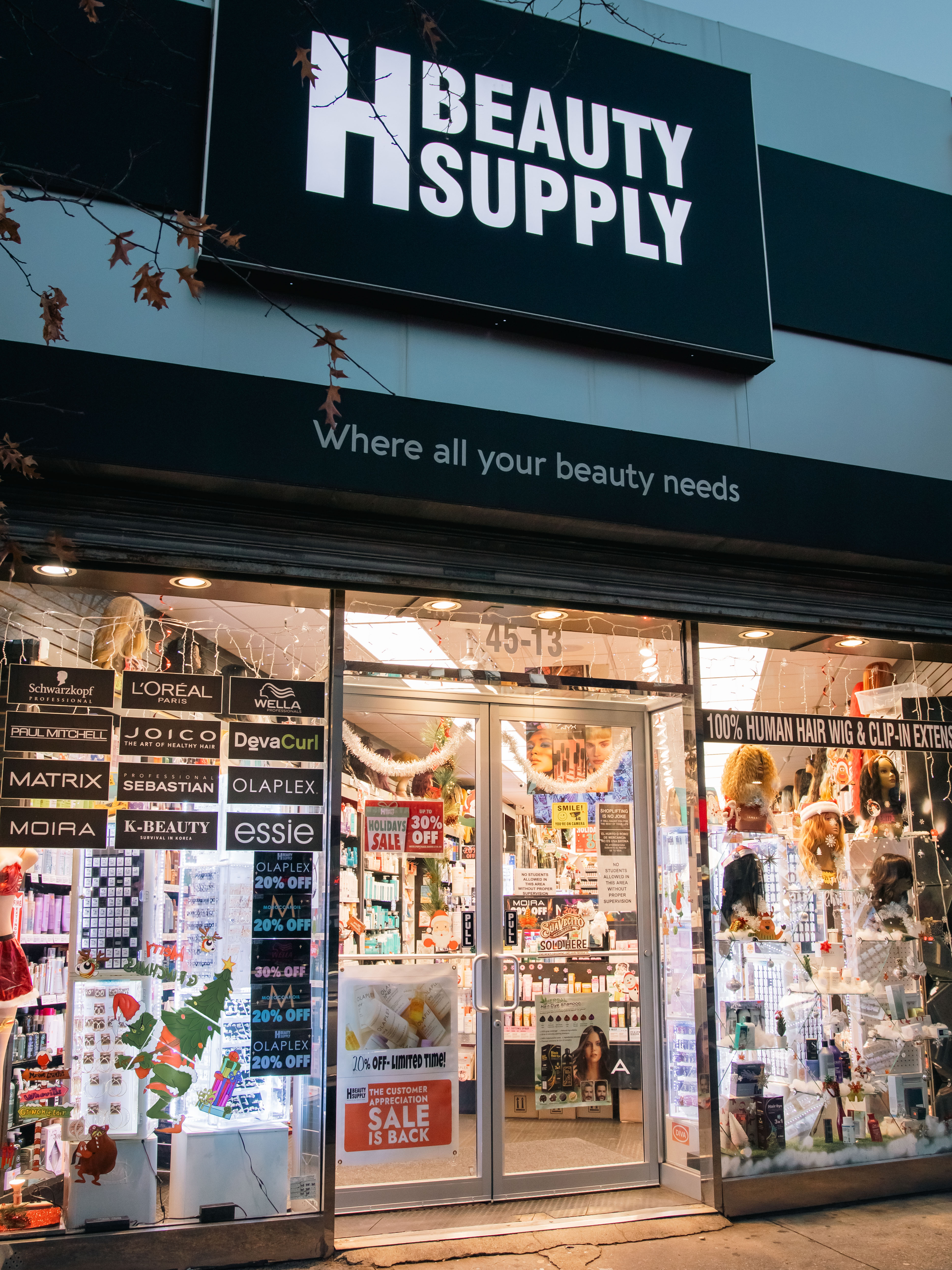 Exterior view of H Beauty Supply store, featuring large signage and product displays in windows, illuminated at night.